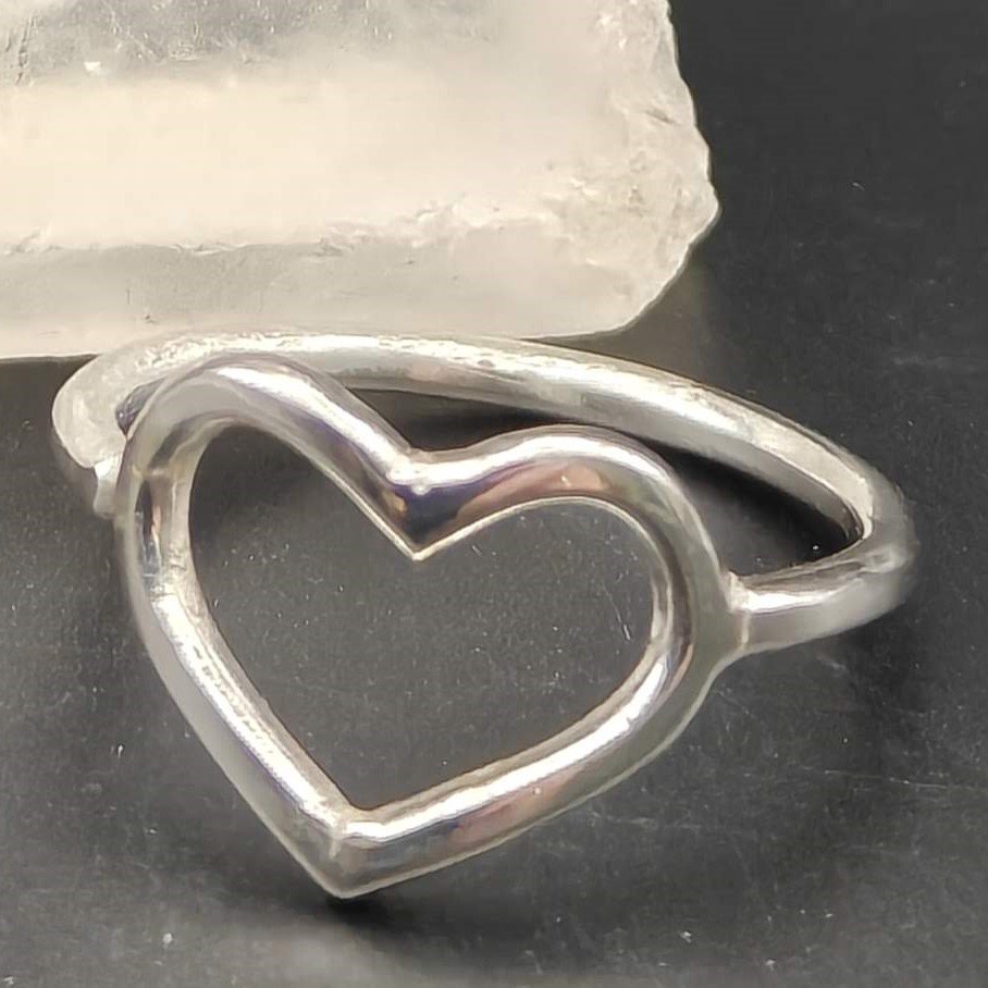Hand-made sterling silver heart ring resting on a wooden workbench